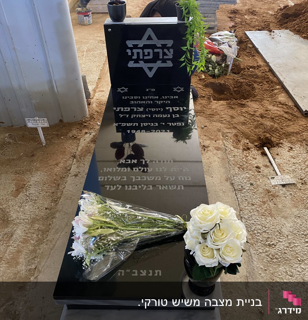 מצבה שחורה עם כיתוב בעברית ופרחים לבנים